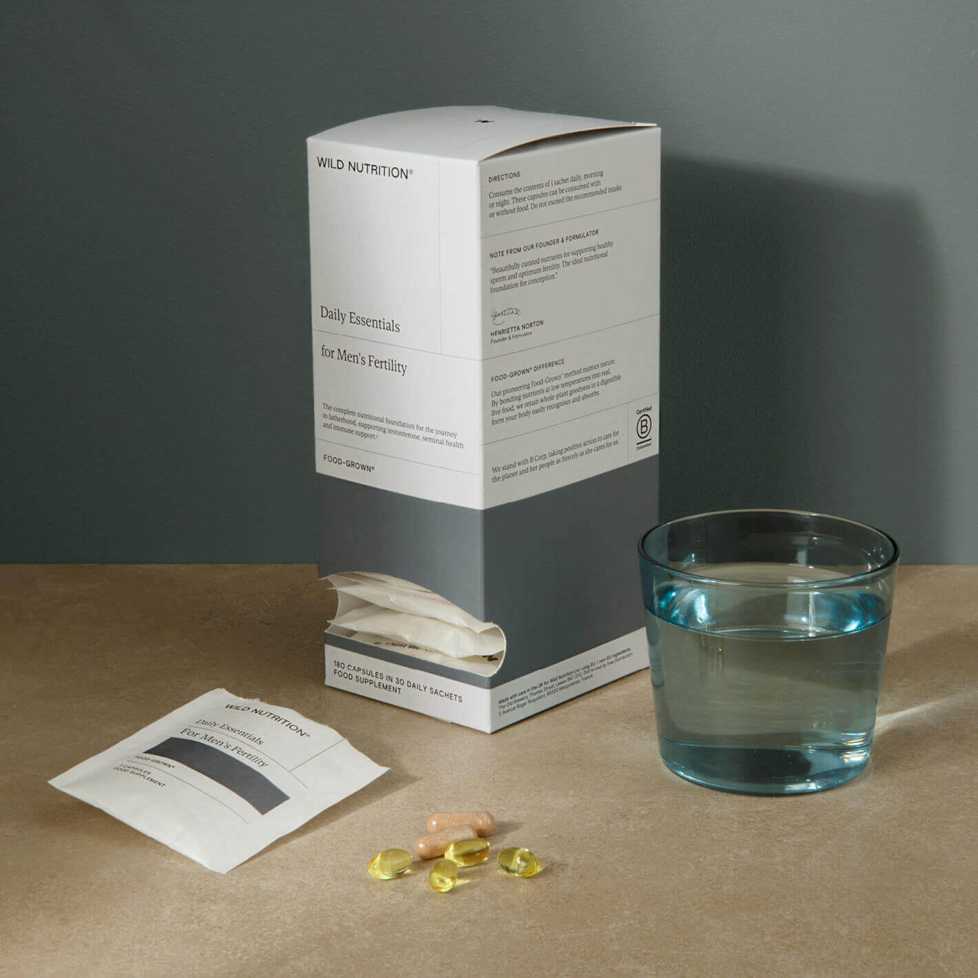 Daily essentials for men's fertility with supplements, sachets, and a glass of water on a countertop.