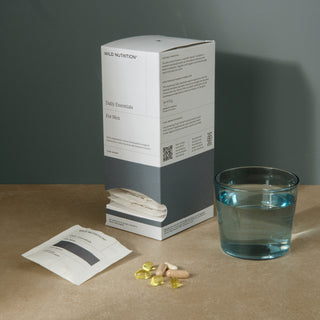 Wild Nutrition Daily Essentials for Men box with sachets, supplement capsules, and a glass of water on a minimalist surface.