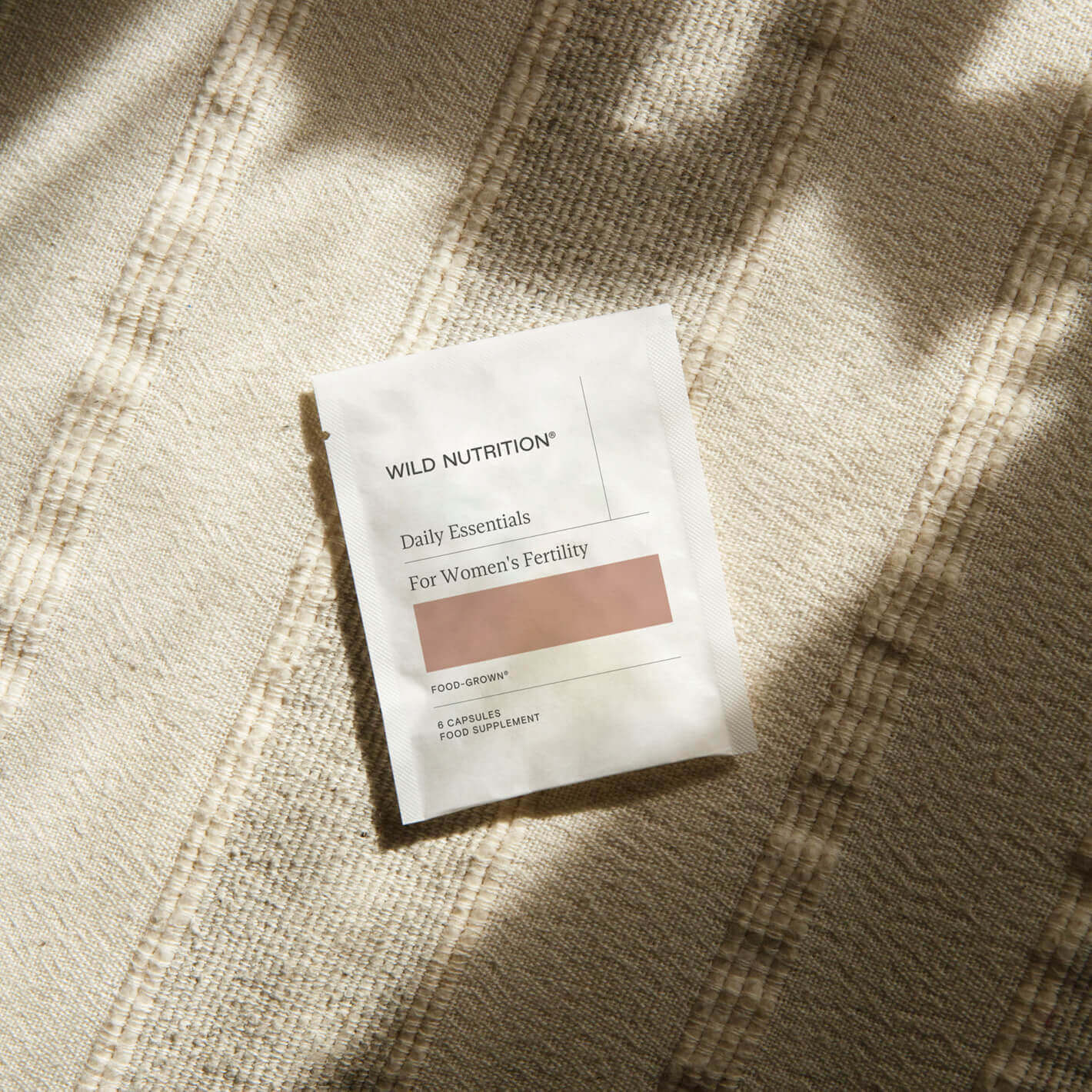 Daily Essentials sachet by Wild Nutrition for women's fertility support on a textured surface.