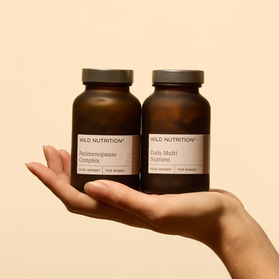 Hand holding Wild Nutrition Perimenopause Complex and Daily Multi Nutrient supplements for women in amber glass bottles