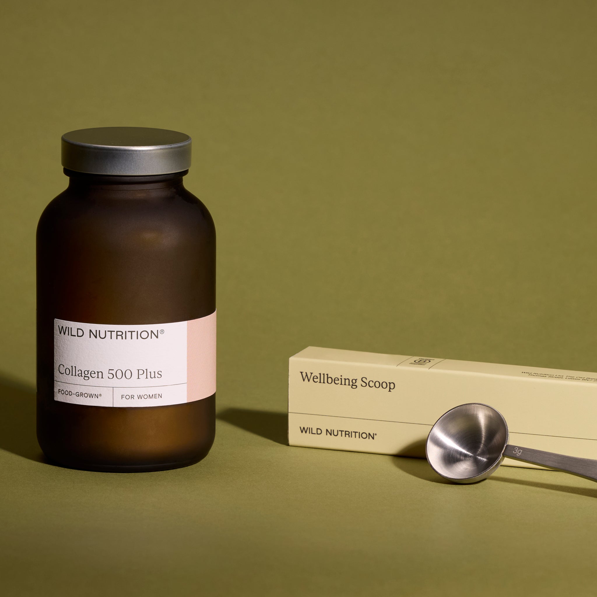 Wild Nutrition Collagen 500 Plus bottle and Wellbeing Scoop with metal measuring spoon on olive green background