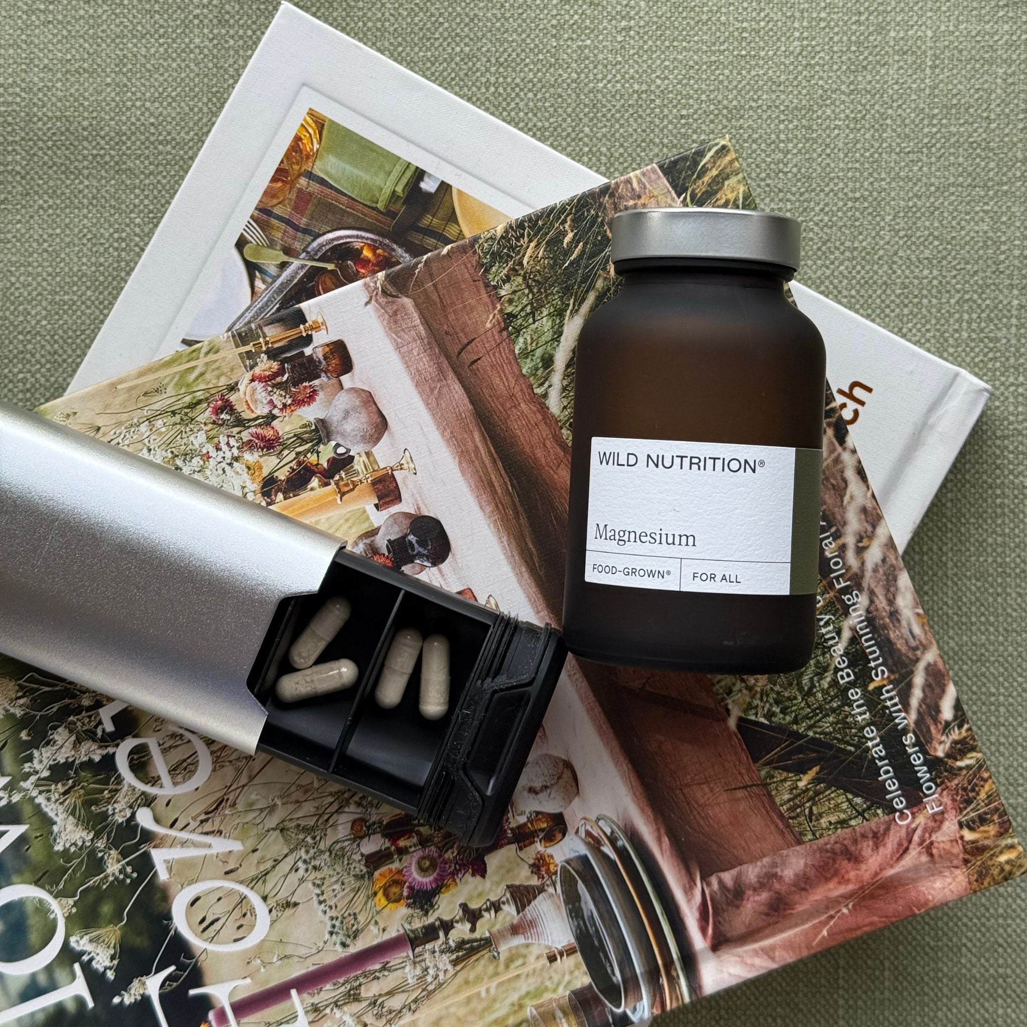 Wild Nutrition Food-Grown Magnesium supplement bottle with capsule dispenser on floral-themed magazines