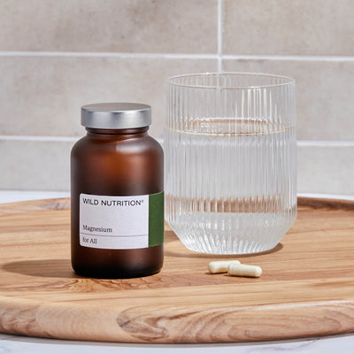 Wild Nutrition Magnesium for All bottle with glass of water and capsules on a wooden tray, promoting heart health.