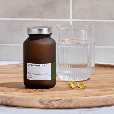 Wild Nutrition Pure Strength Omega 3 supplement bottle with water and omega capsules on a wooden tray.