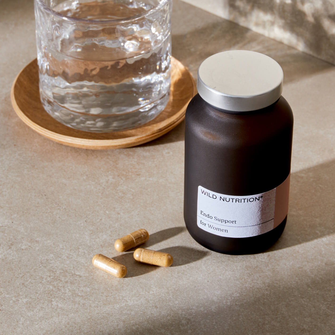 Endo Support Trio capsules beside a glass of water on a stone surface for hormonal and immune support.