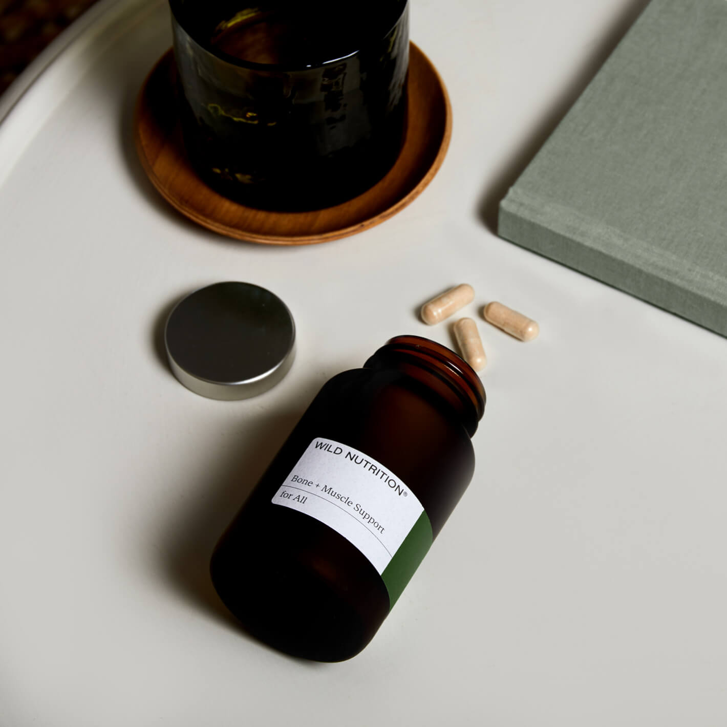 Wild Nutrition Joint + Bone Support supplement bottle next to herbal capsules and a mug on a stylish table.