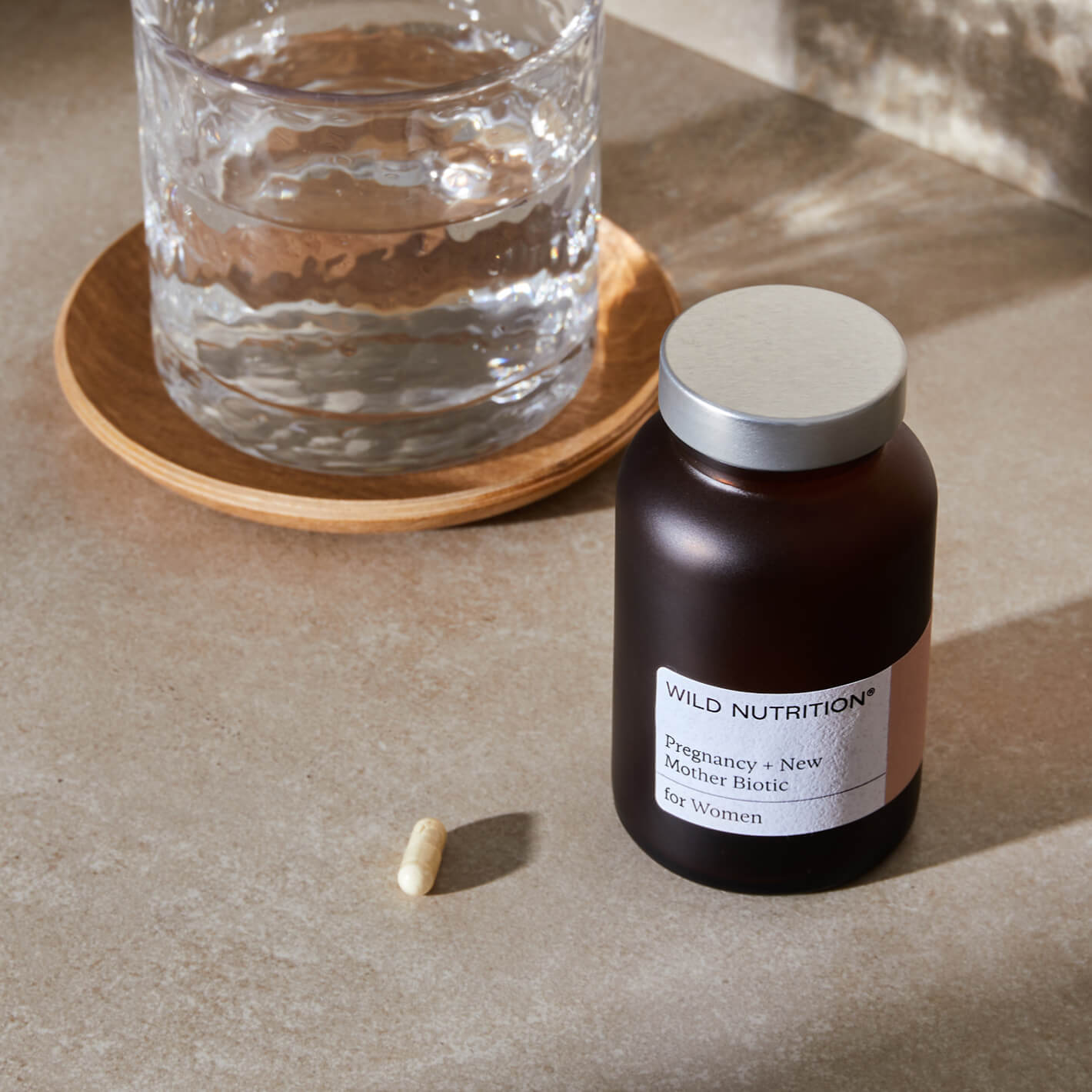 Wild Nutrition Pregnancy + New Mother Biotic supplement bottle next to a glass of water on a table.
