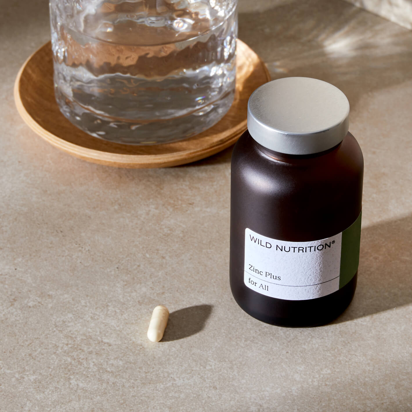 Wild Nutrition Zinc Plus supplement bottle with a capsule and water glass, promoting wellness and health.