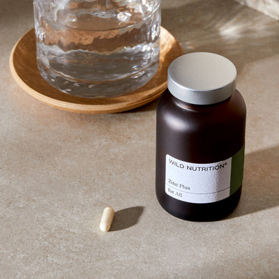 Wild Nutrition Zinc Plus supplement bottle with a capsule and water glass, promoting wellness and health.